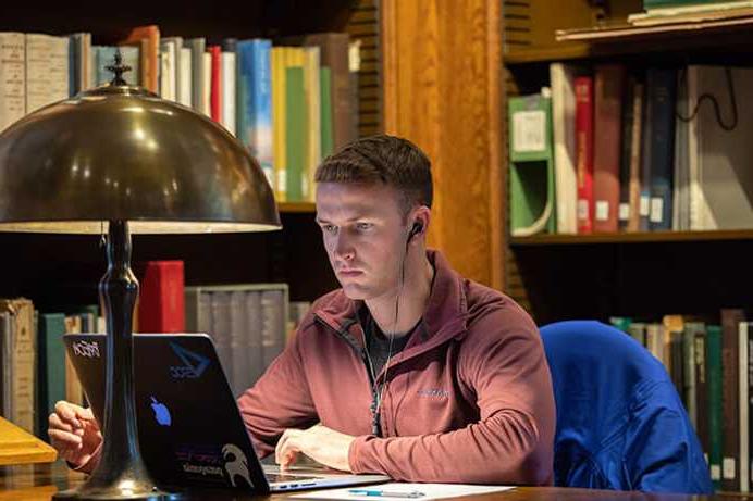 Photo of a Case Western Reserve University School of Law student looking at a computer in a library, wearing headphones